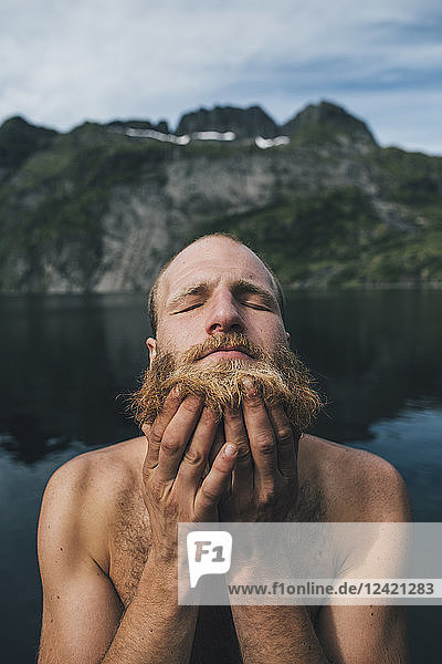 Man washing his beard at a lake with eyes closed