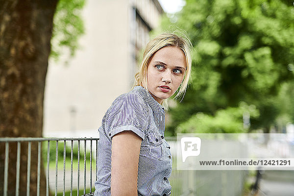 Serious blond young woman at a fence