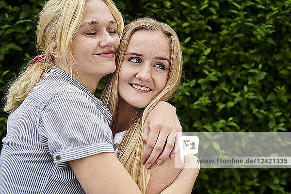Two happy young women hugging a hedge