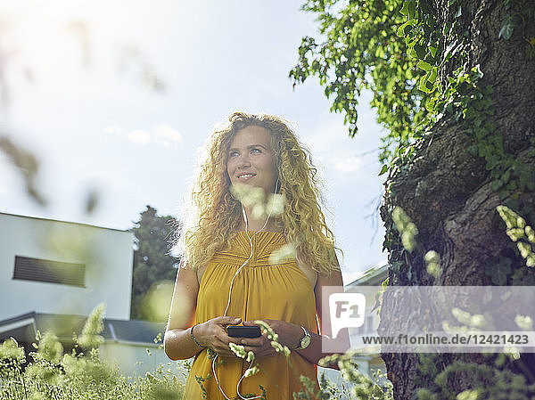 Smiling young woman with cell phone and earphones outdoors