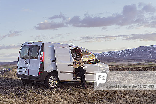 Iceland  young man leaning on van and playing guitar