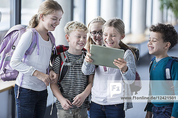 Laughing pupils looking at tablet on school corridor