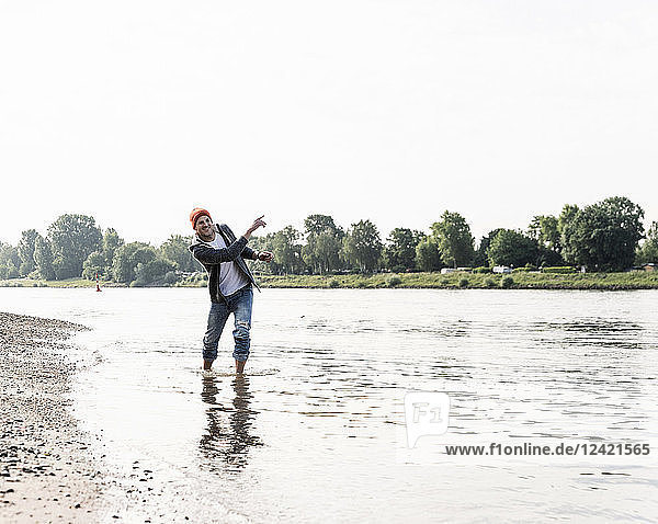 Mature man with red beanie throwing stone into water