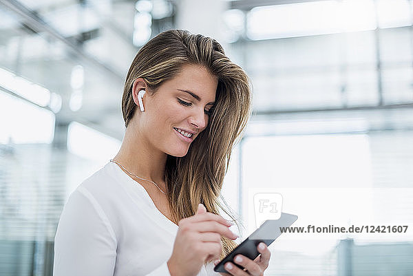 Smiling young woman wearing in-ear phone using cell phone
