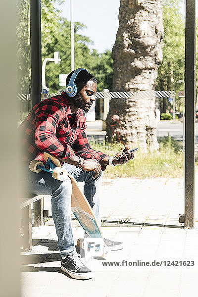 Cool young man with headphones  waiting at bus stop