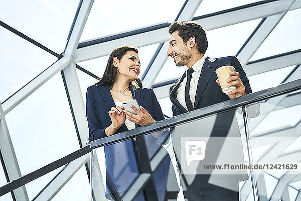 Smiling businesswoman and businessman with coffee and cell phone talking in modern office