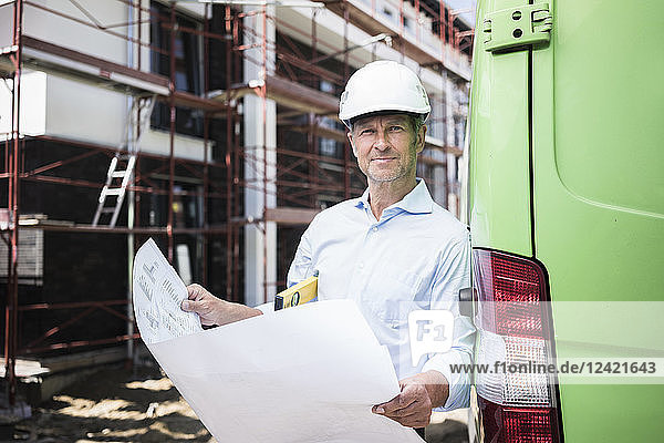 Portrait of architect with blueprint wearing hard hat on construction site