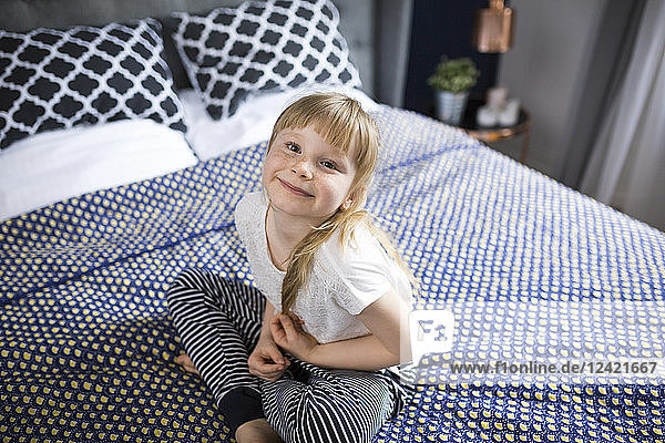 Blond little girl sitting on bed  smiling