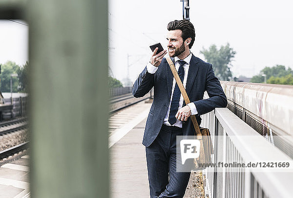 Smiling businessman using cell phone at the platform