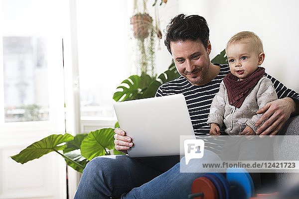father sitting on couch with his little daughter  using laptop