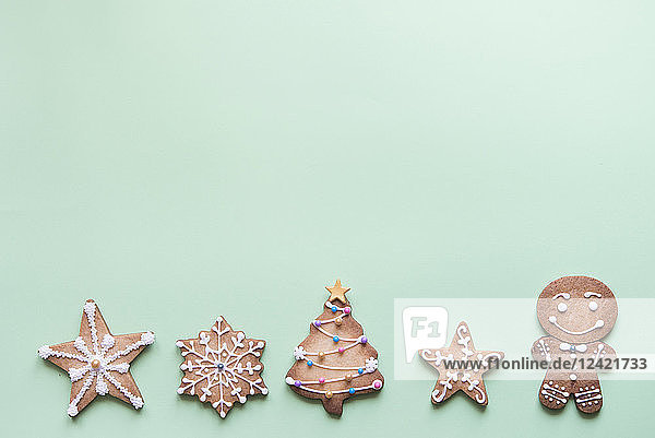 Row of five gingerbread cookies decorated with sugar icing on bright green background