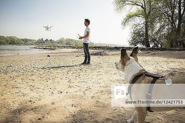 Man with a dog flying drone at a river