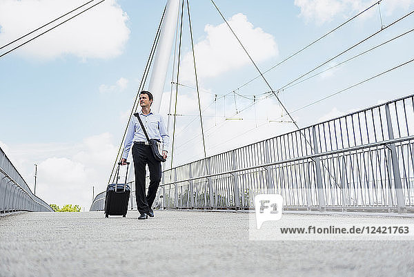 Businessman with rolling suitcase crossing a bridge