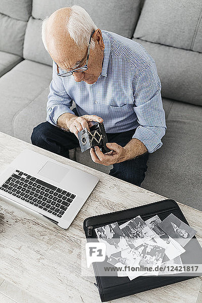 Senior man using laptop and holding his old photo camera  old photos on laptop case