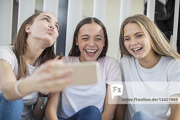 Happy teenage girls sharing cell phone in school