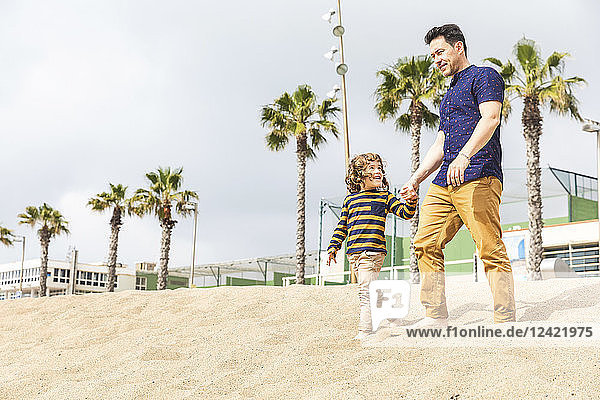 Spain  Barcelona  father and son walking hand in hand on the beach