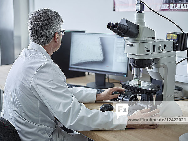 Physician working with microscope  looking on screen