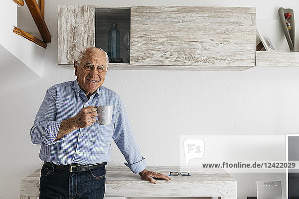 Senior man having a coffee while relaxing at home  looking at camera