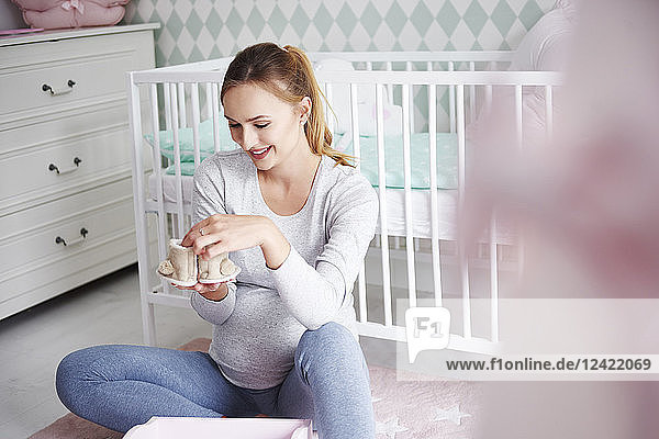 Pregnant woman with baby shoes in baby room