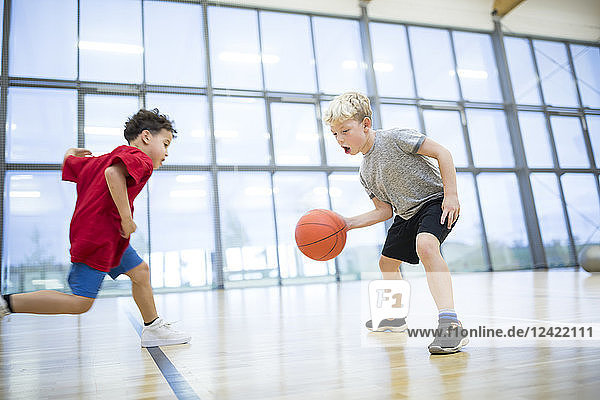Two schoolboys playing basketball in gym class