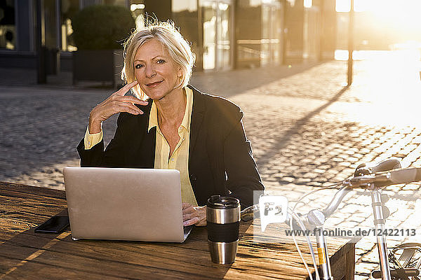 Smiling senior businesswoman using laptop in the city at sunset