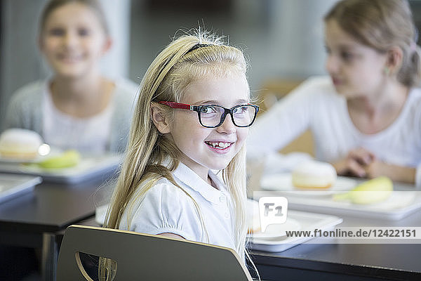 Portrait of smiling schoolgirl with classmates in school canteen