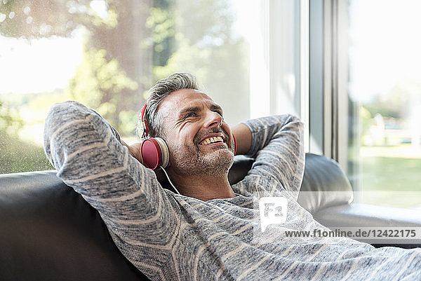 Happy mature man lying on couch at home wearing headphones