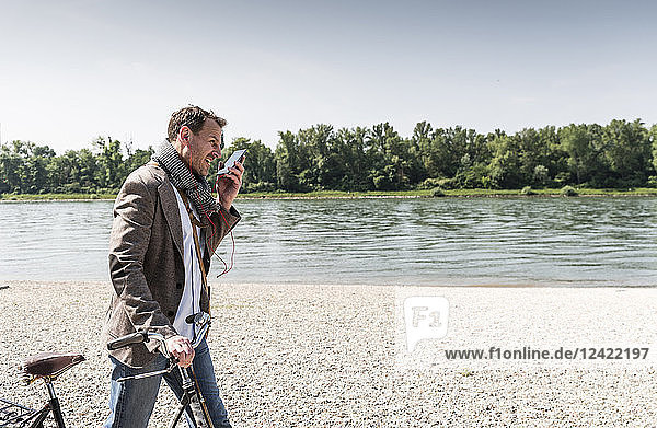 Mature man with bike using smartphone at Rhine riverbank
