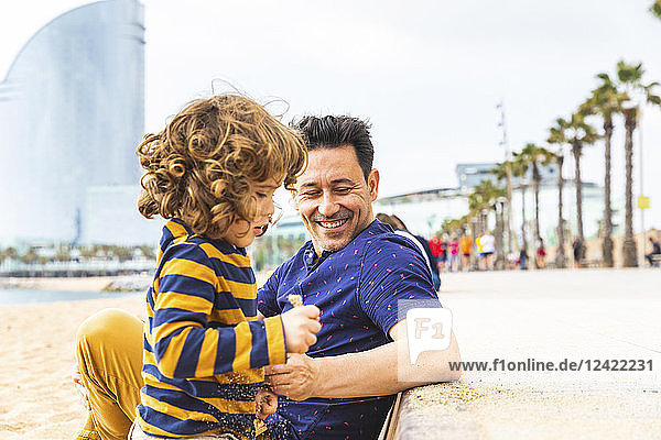 Spain  Barcelona  young boy playing with sand  his father sitting next to him and smiling
