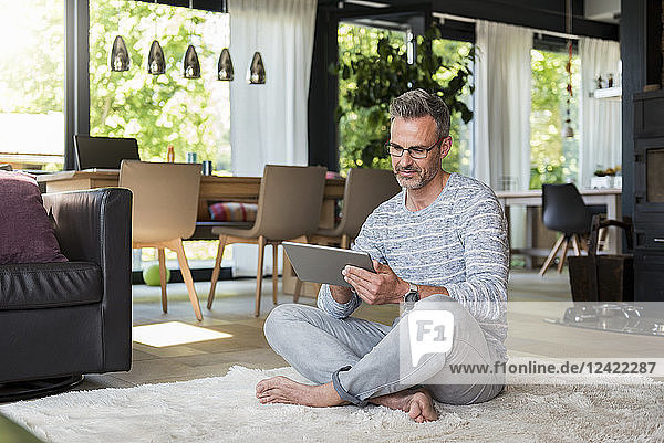 Mature man sitting on carpet at home using a tablet