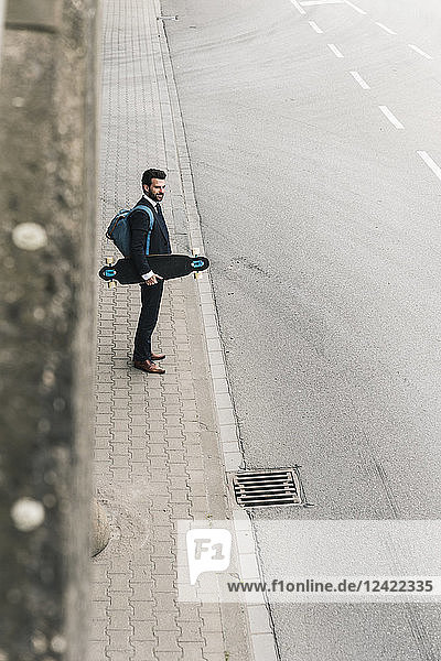 Businessman carrying skateboard standing at the street