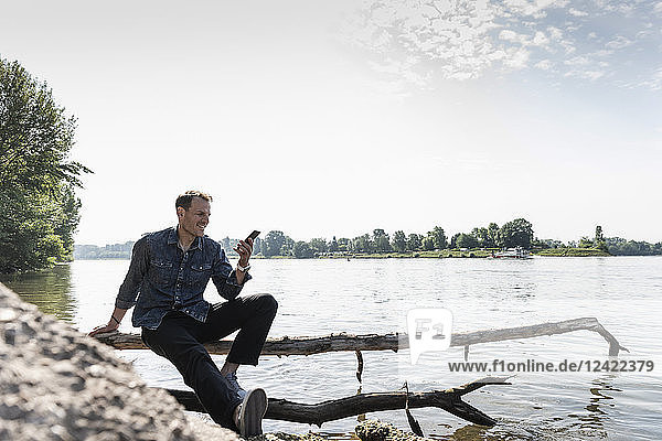 Mature man sitting at Rhine riverbank  using smartphone