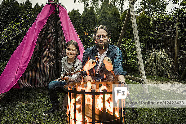 Father and daughter grilling twist bread over camp fire