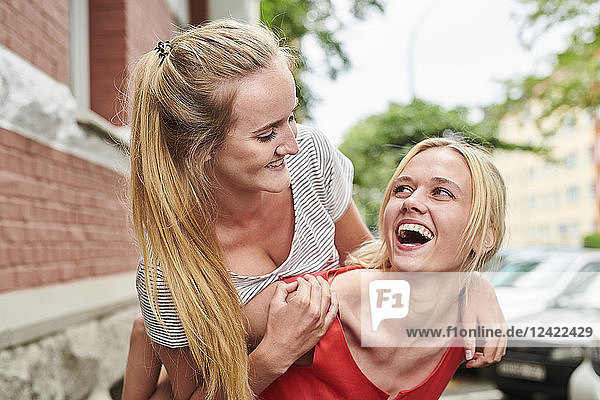 Happy young woman giving friend piggyback ride in the city