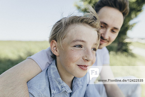 Portrait of young man embracing smiling boy at a field