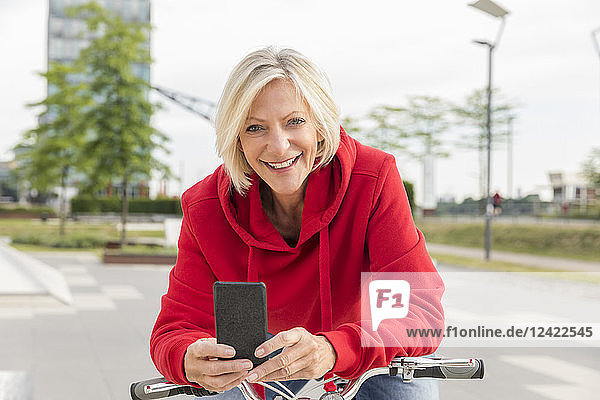 Portrait of smiling senior woman with city bike and cell phone