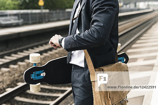 Close-up of businessman with skateboard waiting at the platform
