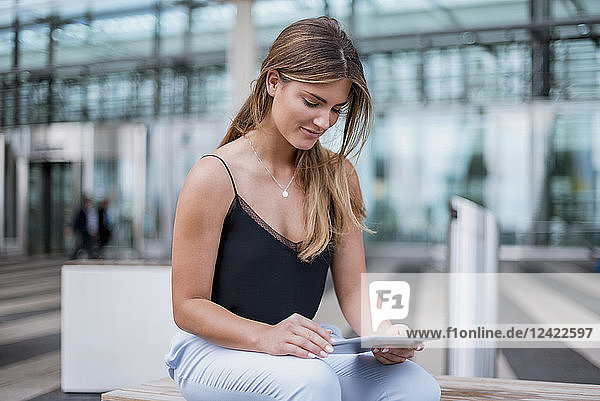 Smiling young woman sitting outdoors using tablet