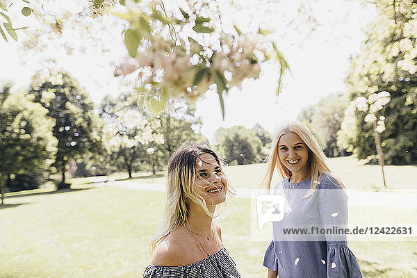 Two happy young women in a park at blossoming tree