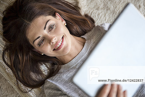 Smiling woman lying on carpet using a tablet
