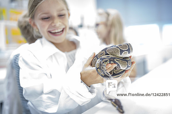 Happy schoolgirl in science class holding snake