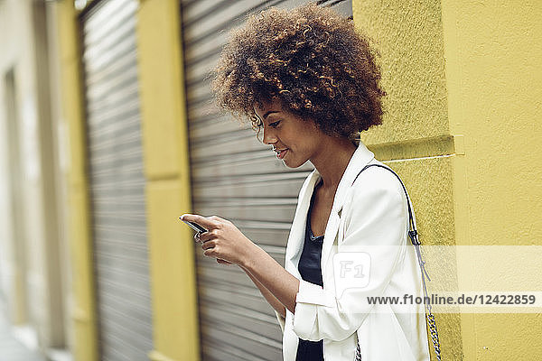 Smiling young woman with curly hair looking at cell phone