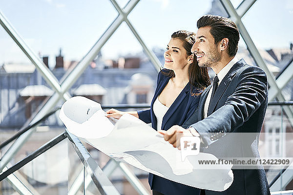 Smiling businesswoman and businessman holding plan in office