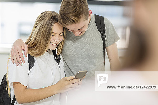 Boy embracing girl in school and looking at cell phone together