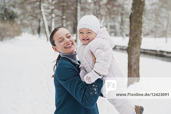 Portrait of happy baby girl having fun with her mother in snow-covered landscape