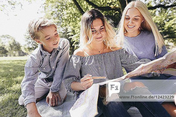 Two young women and a boy looking at map in a park
