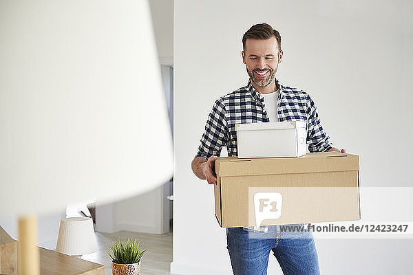 Happy man moving into new flat carrying cardboard box