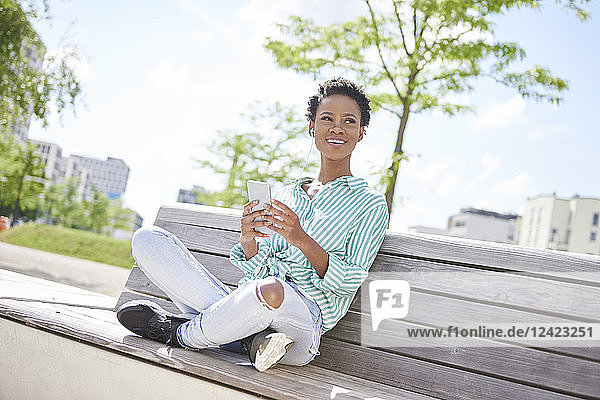 Portrait of smiling young woman with cell phone and earphones sitting on bench