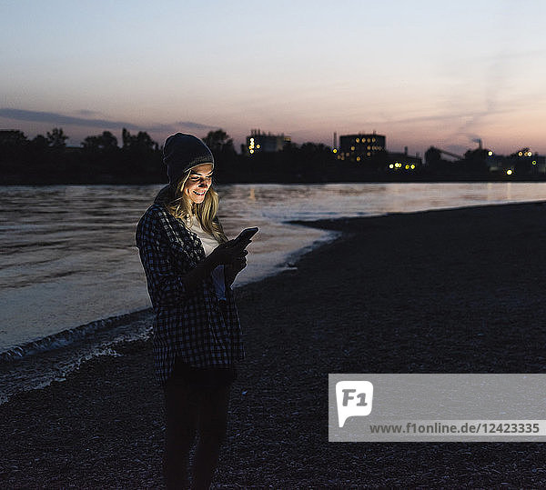 Young woman using smartphone on riverside in the evening