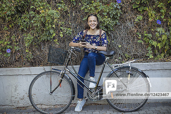 Portrait of smiling teenage girl with cell phone and bicycle